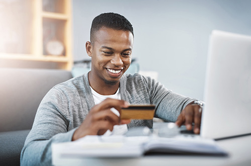 young African-American male using laptop and holding credit card, credit card basics, digital banking