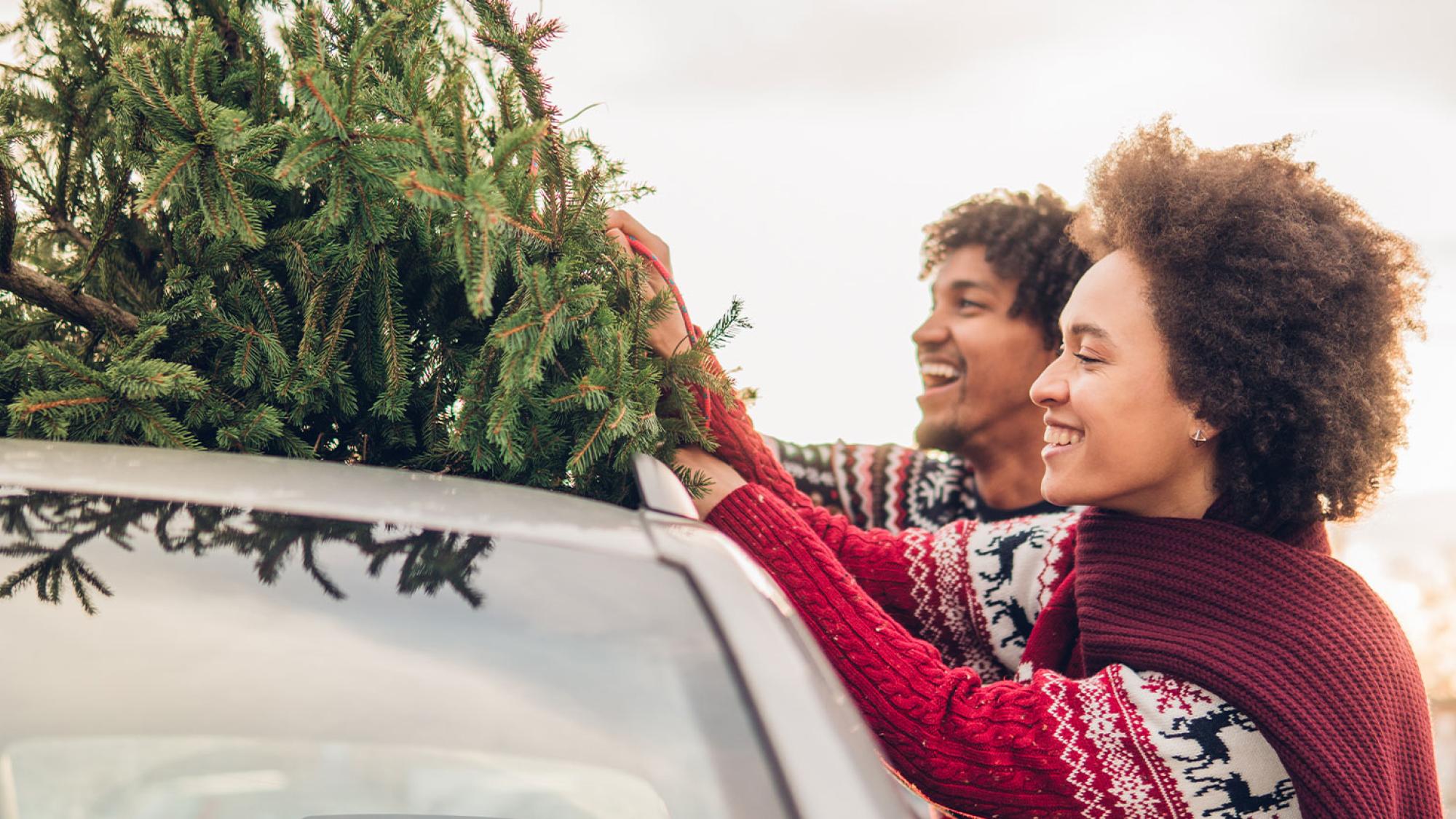 Man and woman putting christmas tree on top of car