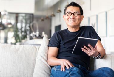 A happy man sitting on a couch holding his tablet smiling