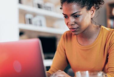 young African-American woman sitting at computer looking at screen, online activity, online fraud, scams, email, phishing, wire transfer scams