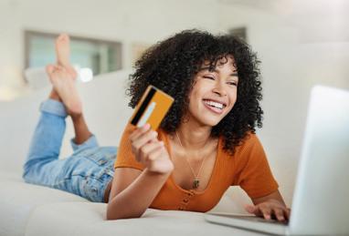 young African-American woman on couch using laptop holding credit card, credit card, credit card rewards, online shopping, making the most of your credit cards