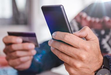close up of man holiday shopping online, holding smartphone and credit card, holiday decorations, holiday sweater, online shopping, online fraud, holiday scams