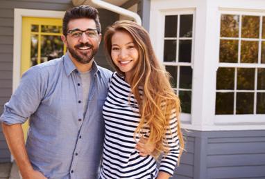 young couple standing in front of new home, first home, buying a home, buying your first home, home buying, home buying tips