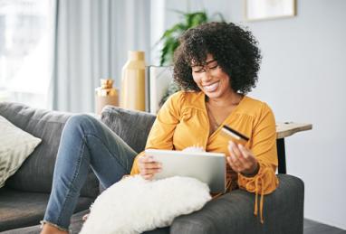 young black woman sitting on couch at home holding credit card and tablet, credit card, first credit card, getting your first credit card, credit score, credit card application