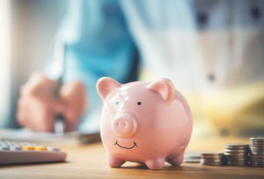 piggy bank sitting on table with stacks of coins next to it and a calculator, person in background, creating a savings plan, saving money 