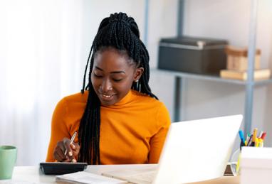 young Black woman using calculator sitting at computer, filing taxes, tax return, tax refund, how to make the most of your tax refund 