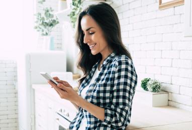 young white woman smiling in kitchen using smartphone, digital banking, account protection