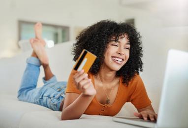 young black woman laying on couch holding credit card and using laptop, common credit myths