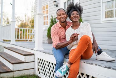 young adult black couple smiling and sitting on front porch of their new home, buying a home, home buying, new home