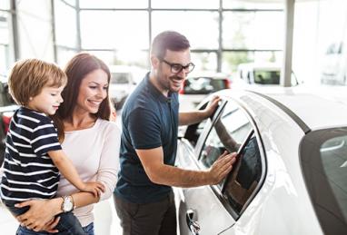 young white family with father and mother holding son shopping for a new car in a showroom at a car dealership, car shopping, car buying, buying a car 