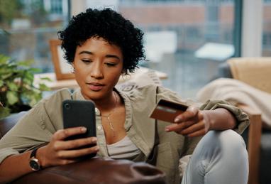 young mixed-race woman sitting at home holding credit card and cell phone, reporting card fraud, recovering from card fraud