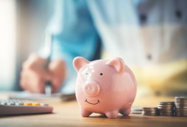 piggy banks sitting next to stacks of coins and calculator, blurred background of a person doing financial calculations, savings calculator, how much should I be saving 