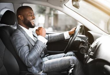 professional black business man in suit driving car with smile on his face and fist in the air in excitement 
