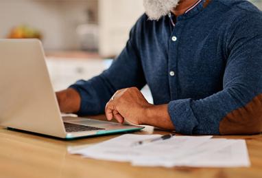 mature black man using laptop to file his taxes, reviewing finances, paperwork