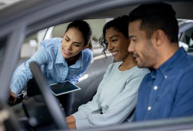 Saleswoman working at a dealership showing a car to a happy couple and trying to make a sale 