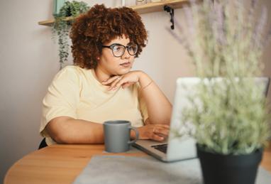 attractive happy stylish plus size African-American woman student afro hair in glasses studying online working on laptop computer at home office workspace