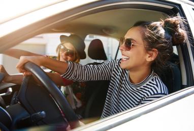 two laughing young girlfriends driving together in car 