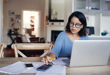 Shot of a young woman using a laptop and calculator while working from home 