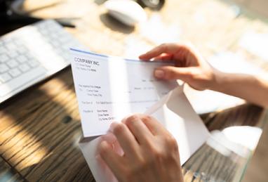 close-up of a businessperson’s hand opening envelope with paycheck over wooden desk