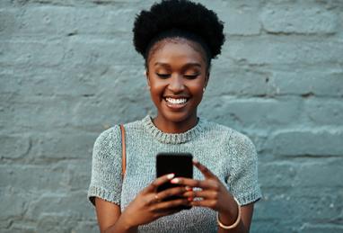 Happy young woman walking on the city street after shopping and using her smartphone