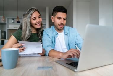 happy Latin American couple at home paying bills online on their laptop and smiling