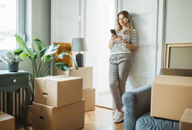 woman moving into new home, resting and using her smartphone 