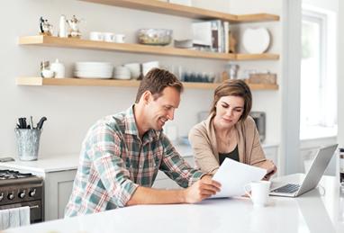 shot of a couple using a laptop while going through paperwork together at home