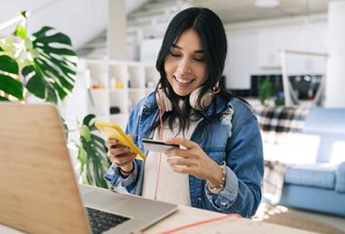 young Hispanic woman doing online shopping at home with credit card and smartphone