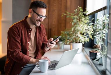 man in stylish casual clothes using smartphone and laptop for electronic banking