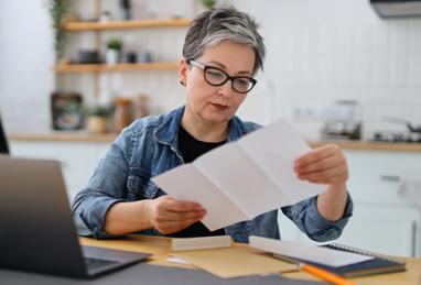 Serious mature woman in glasses reading over her credit report in the kitchen
